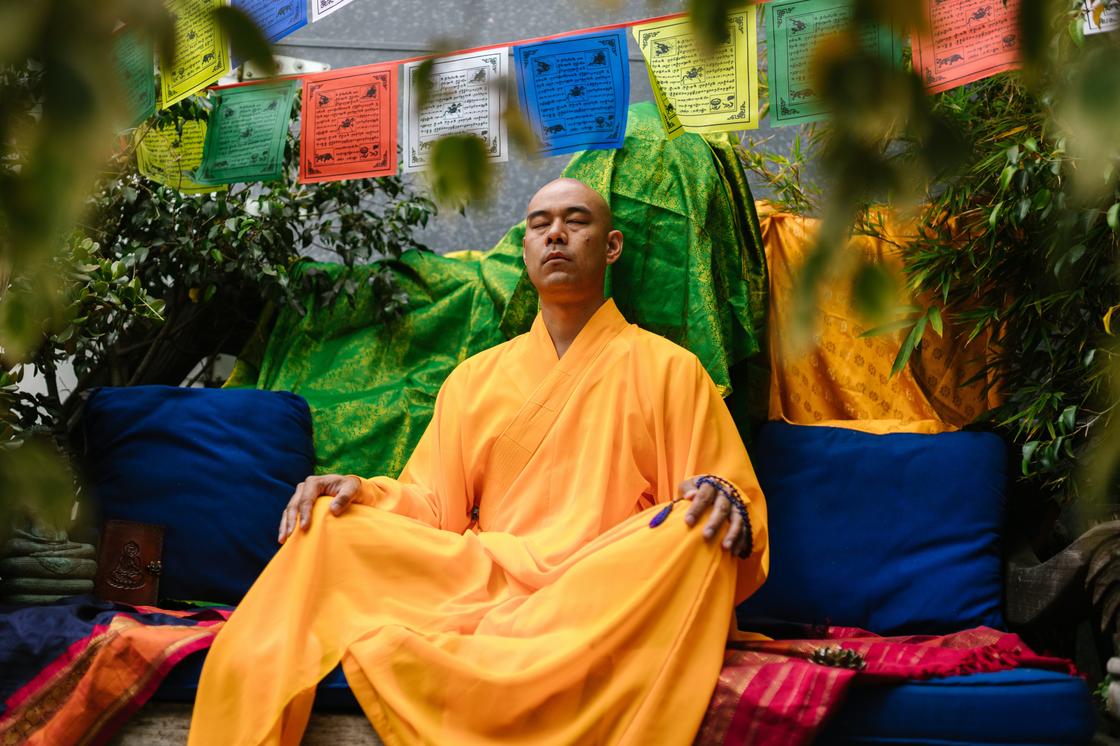 Мужчина в одежде буддийского монаха медитирует, сидя на тахте