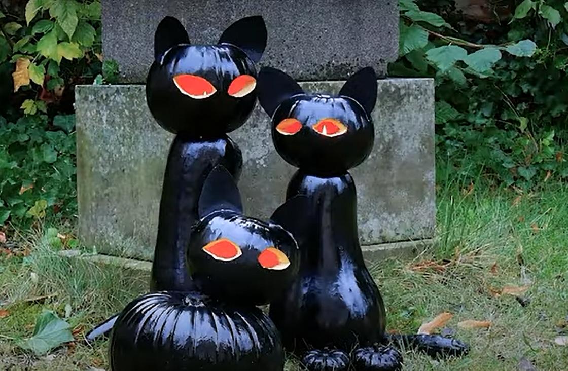 Черные коты, сделанные из тыквы и покрашенные черной краской, стоят на улице