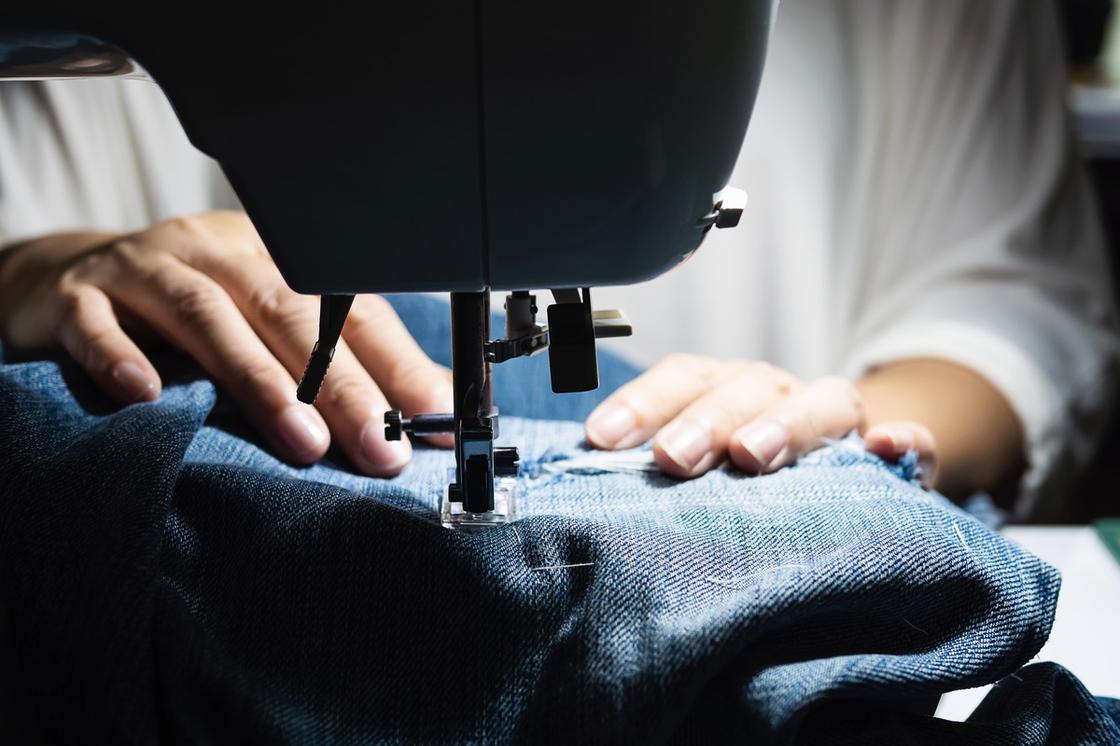 На швейной машинке зашивают дырку на джинсах