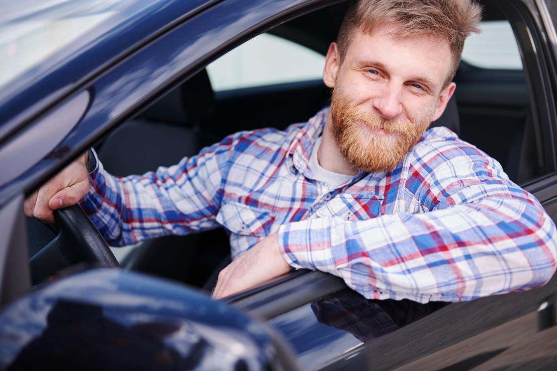 Мужчина в клетчатой рубашке сидит в  машине и улыбается