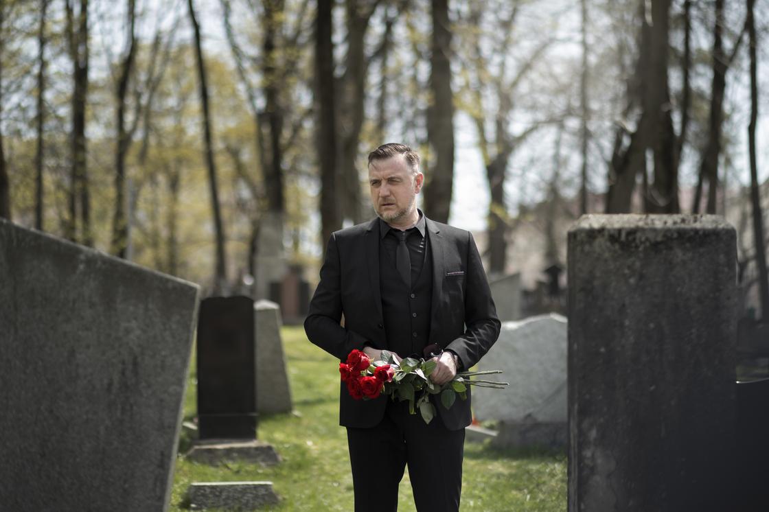 Мужчина с букетом роз стоит между могил