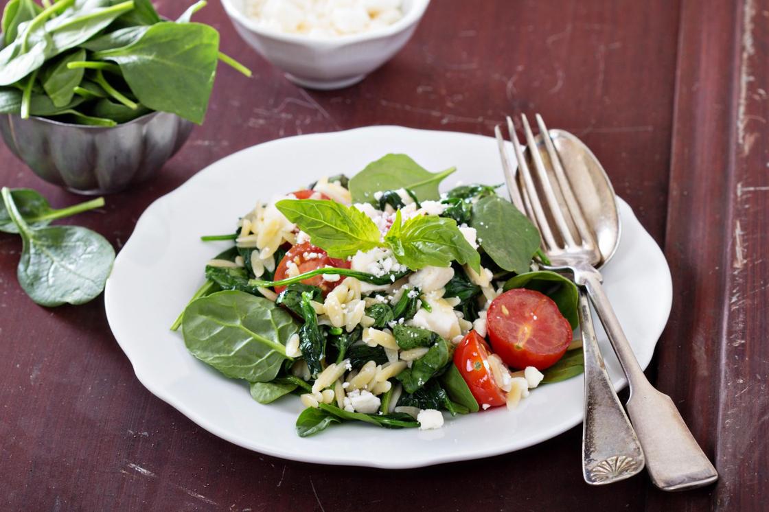 На сервировочной тарелке салат из свежей зелени, феты и пасты орзо
