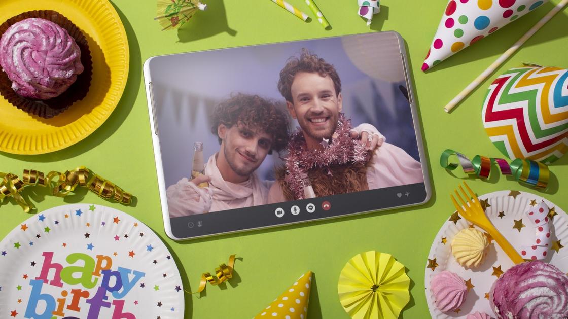 На планшете фотография двух друзей. Рядом с планшетом лежат цветные колпачки, бумажные тарелки с пирожными