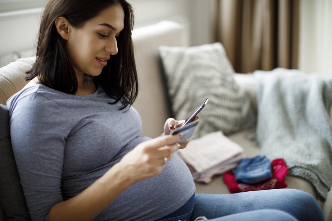 Беременная женщина смотрит в смартфон и держит платежную карту