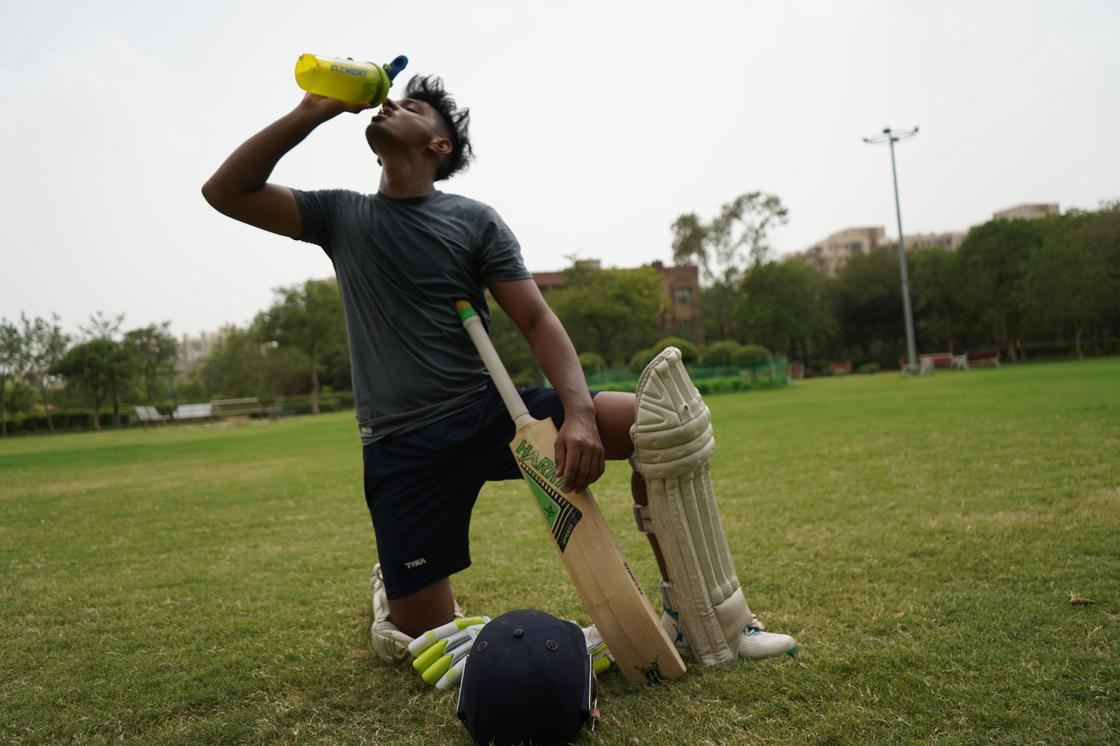 Игрок в крикет пьет воду из пластиковой желтой бутылки