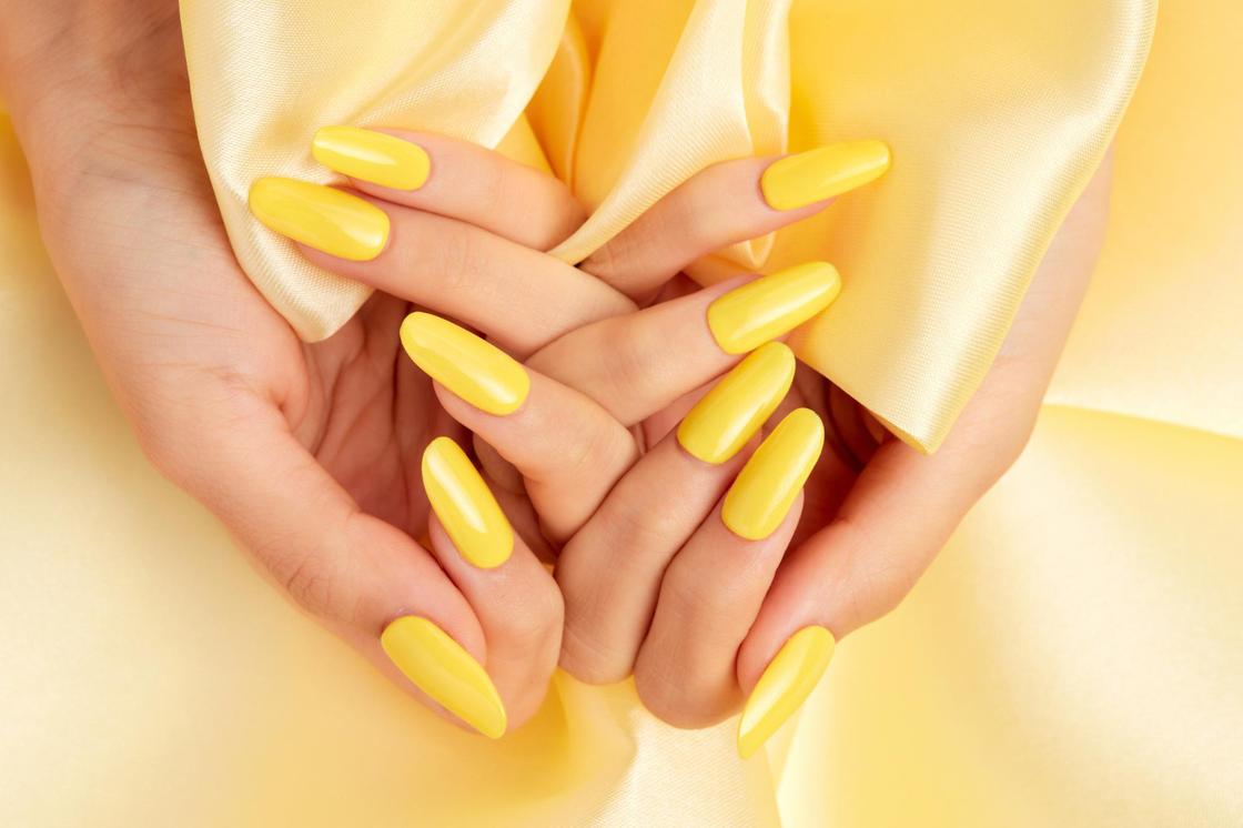 Длинные овальные ногти накрашены ярко-желтым лаком