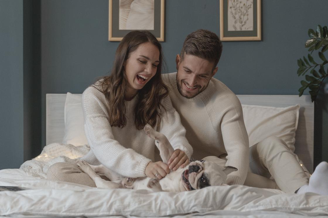 Влюбленная пара играет с собакой на кровати