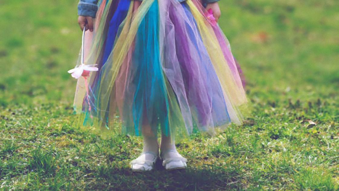 Юбка сделана из разноцветных полосок фатина без шитья одета на девочке, которая стоит на зеленой лужайке с белым цветком в руке
