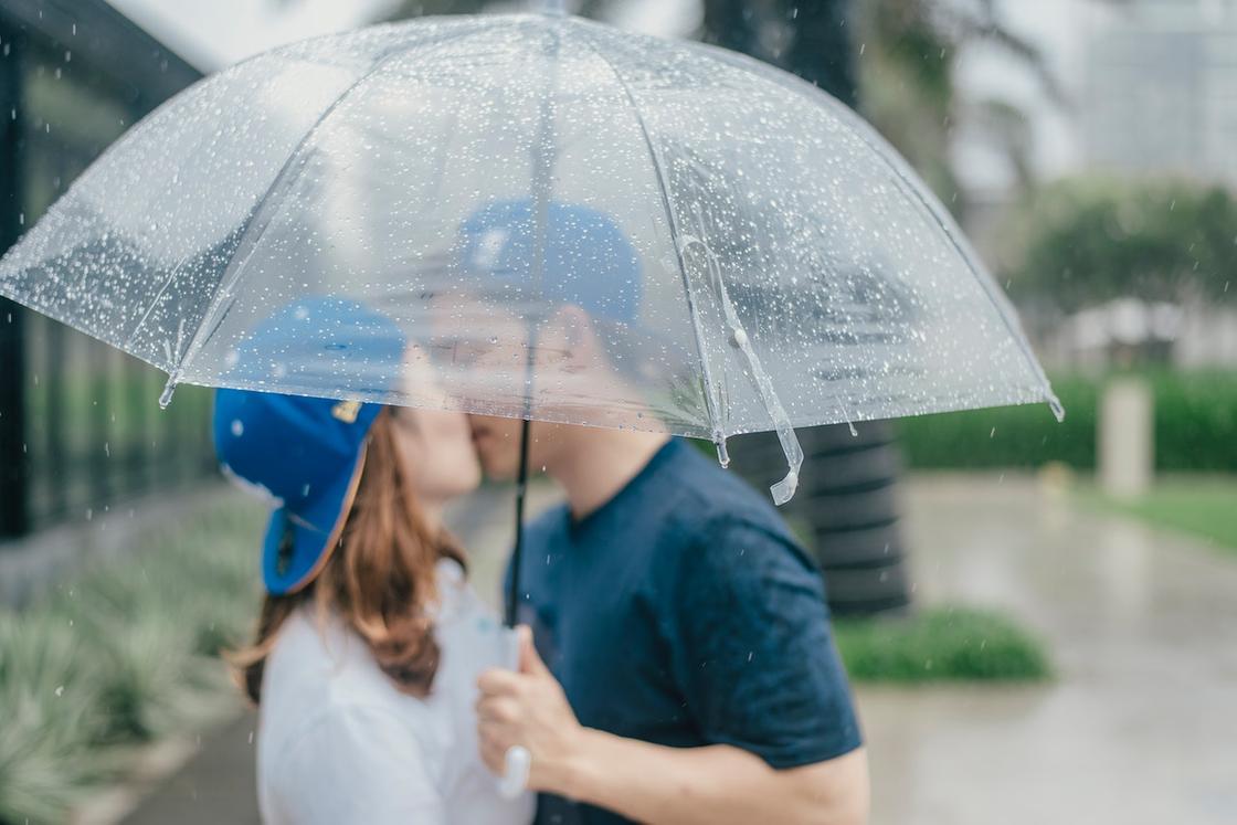 Влюбленные целуются, прикрывшись зонтом от дождя