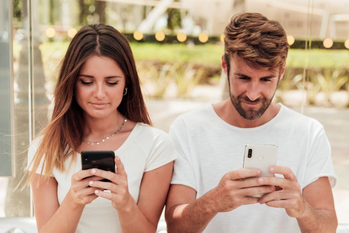 Девушка и парень смотрят на экраны смартфонов