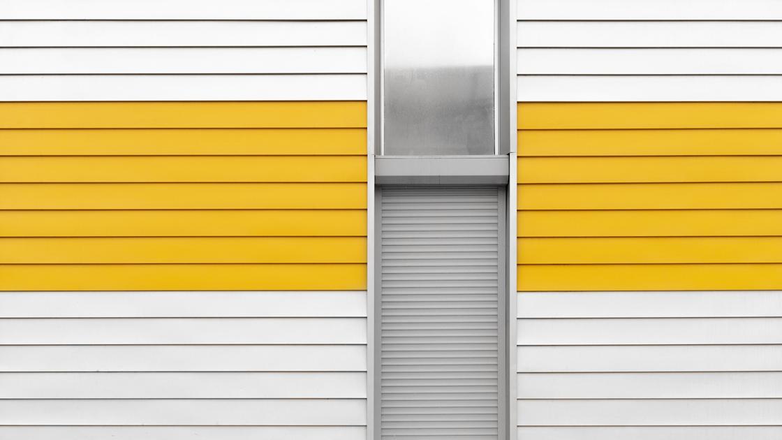 Окно и вход, закрытый жалюзями. Стена покрыта панелями ПВХ белого и желтого цвета