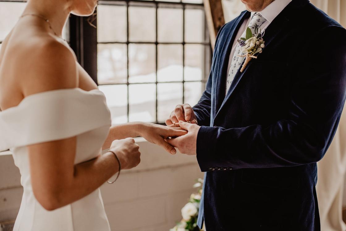 Мужчина надевает обручальное кольцо на палец невесты в белом