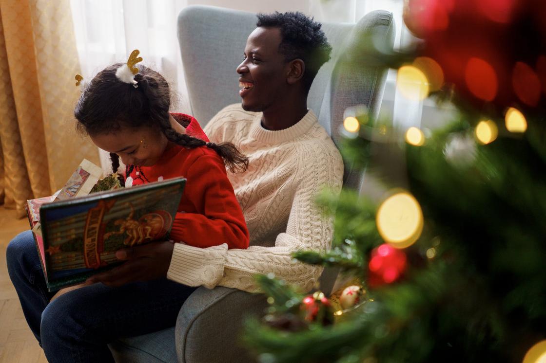 Девочка читает книгу, сидя на руках у улыбающегося отца