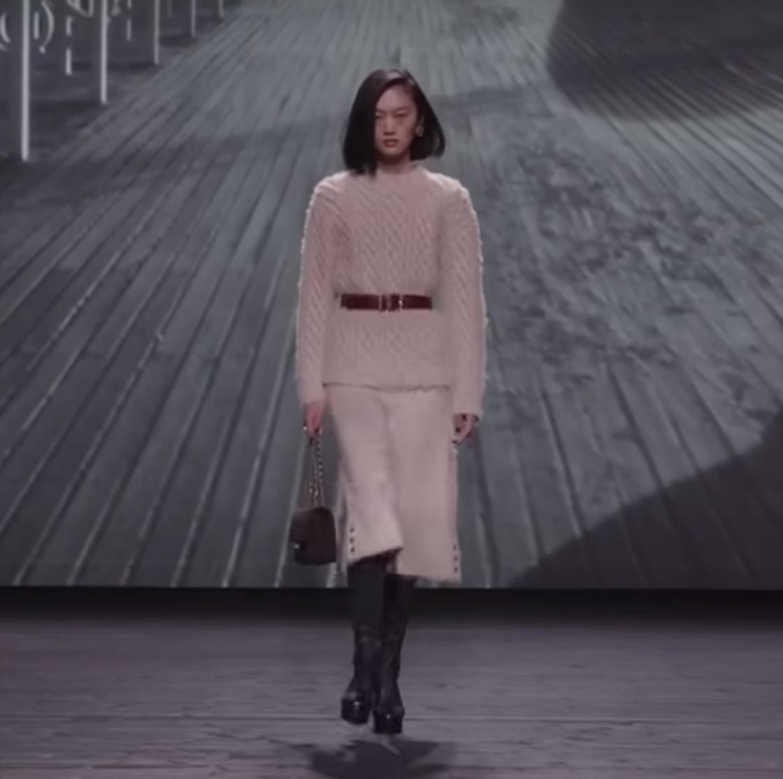 Модель демонстрирует свитер и юбка с поясом на талии от Chanel