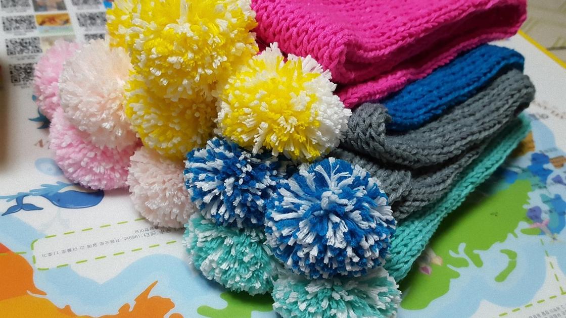 На столе лежат разноцветные детские шарфики с помпонами