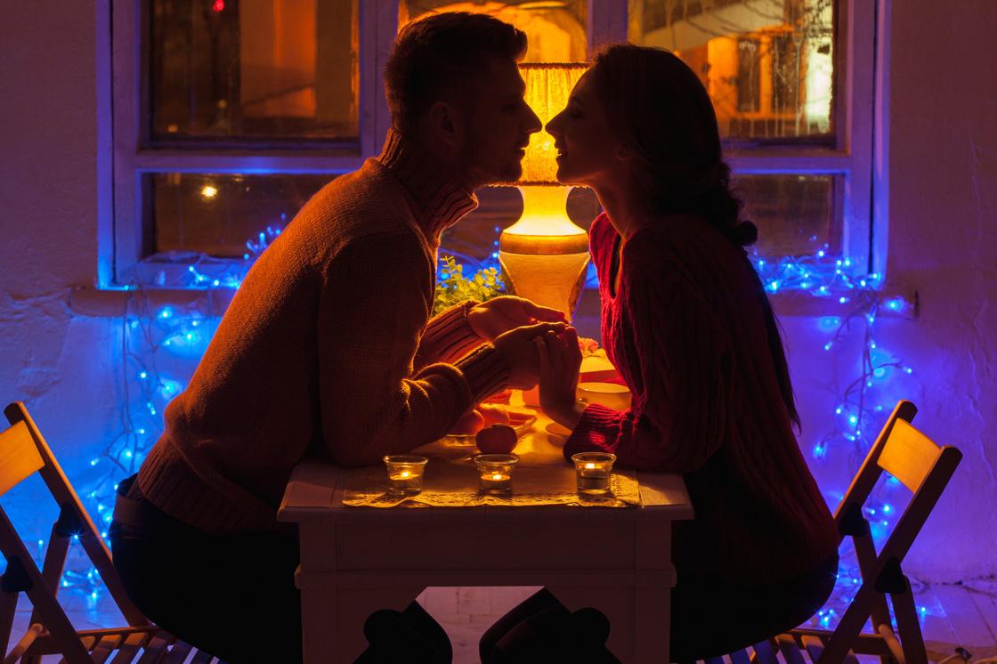 Парень и девушка на романтическом свидании сидят за столиком взявшись за руки