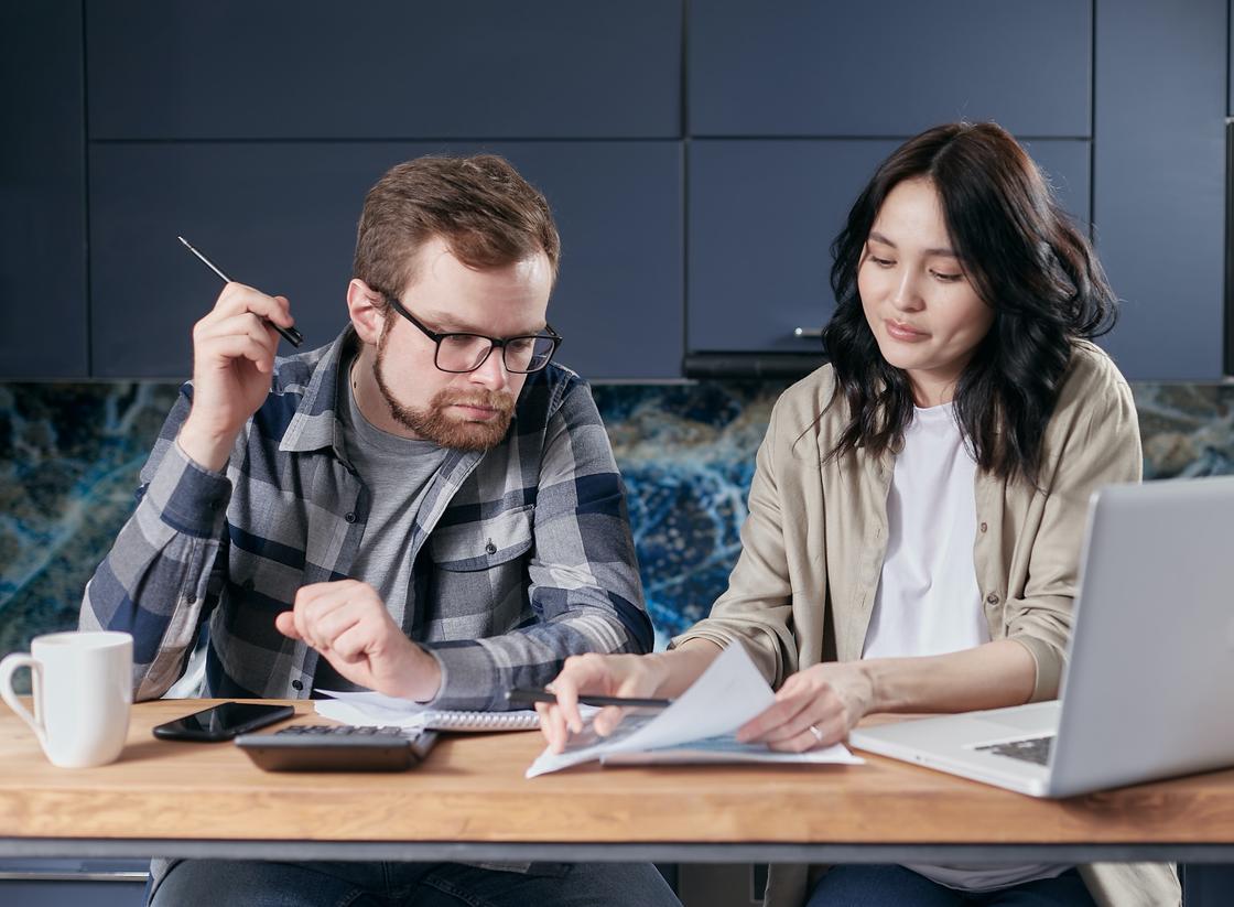 Мужчина и женщина сидят за столом и разбирают бумаги с калькулятором и ноутбуком