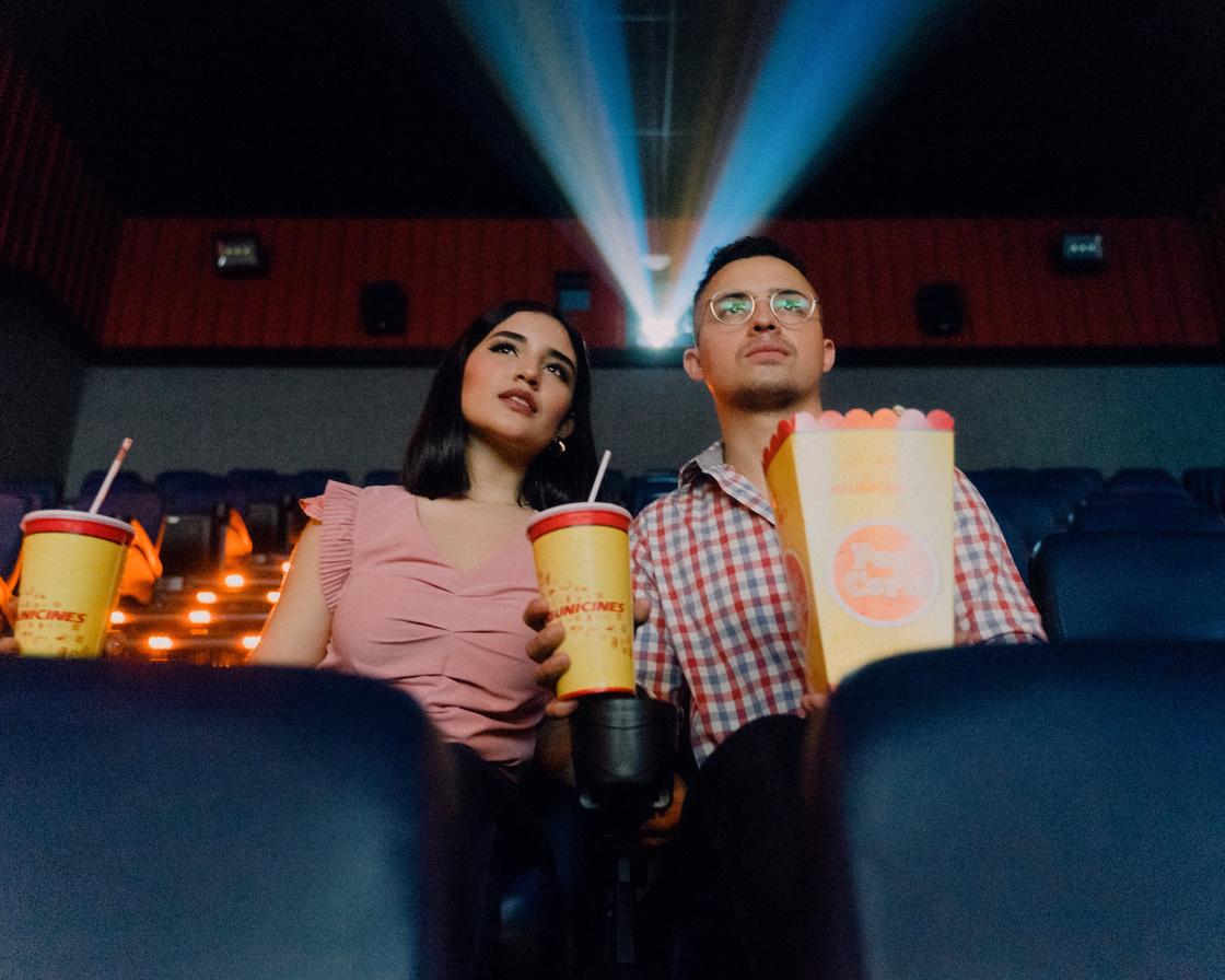 Парень и девушка сидят с попкорном и колой в кинозале