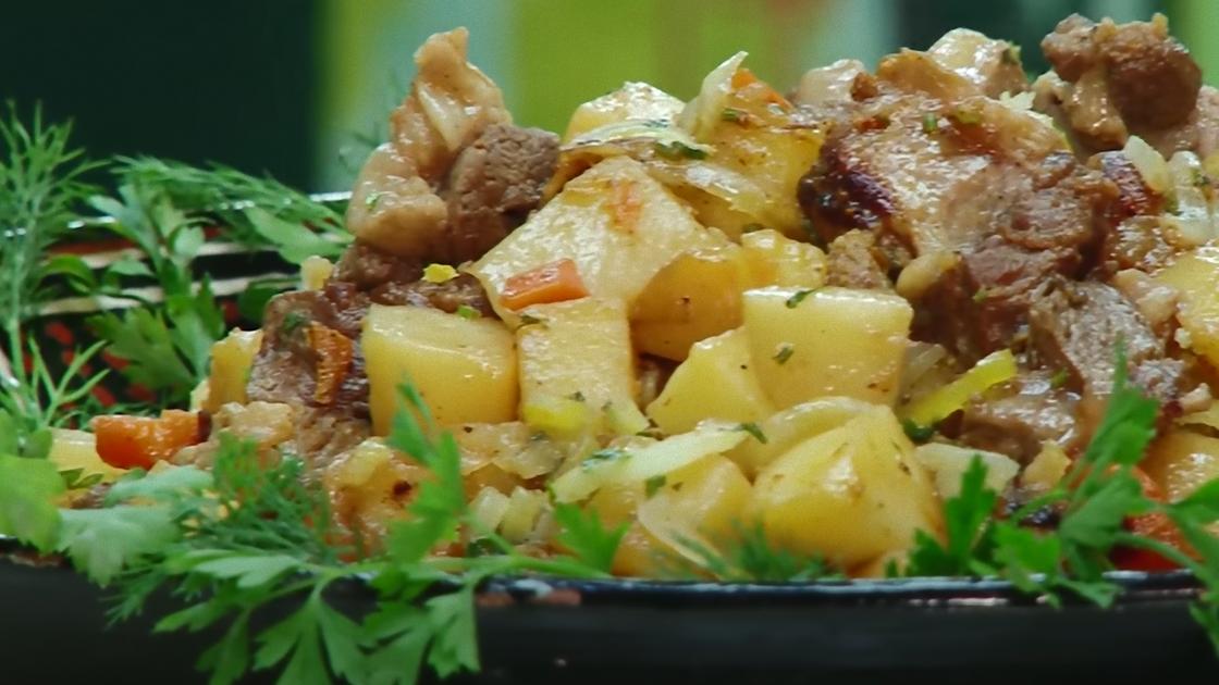 На блюде приготовленные кусочки мяса, картофеля и овощей с зеленью