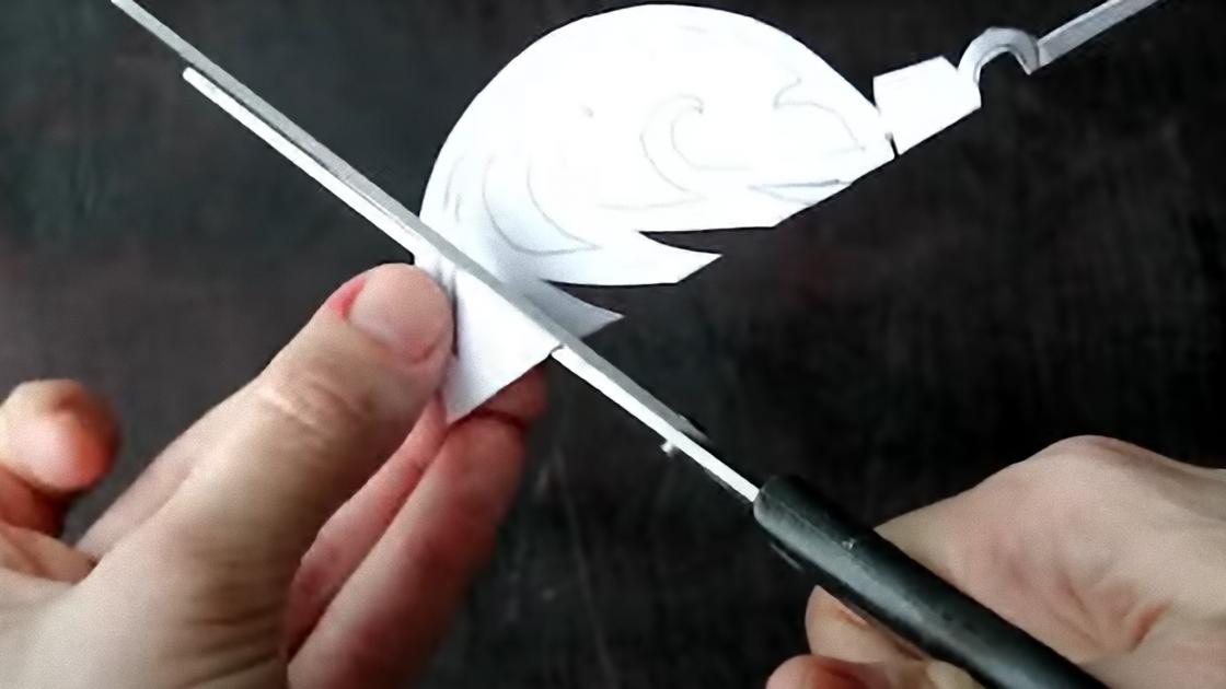 Ножницами вырезают елочную игрушку из бумаги