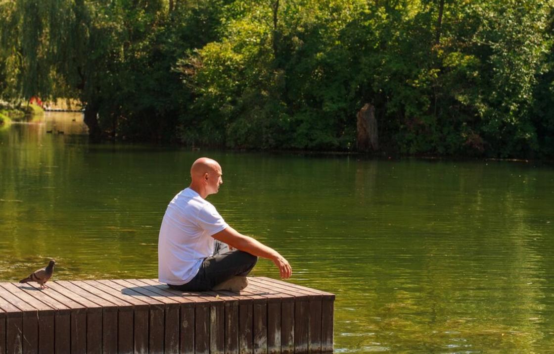 Одинокий лысый мужчина сидит на берегу водоема