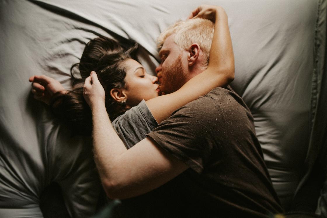 Мужчина и женщина целуются, лежа в кровати обнявшись