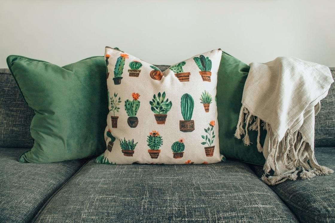 Цветные подушки и плед на диване с серо-зеленой обивкой