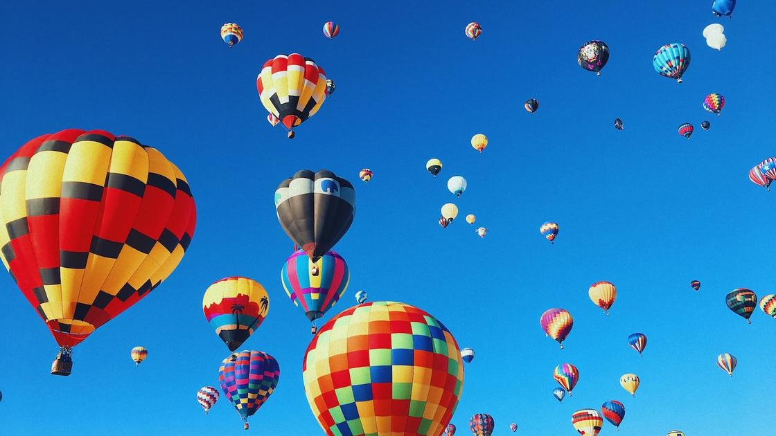 В небо поднимаются яркие разноцветные летательные аппараты в виде воздушных шаров