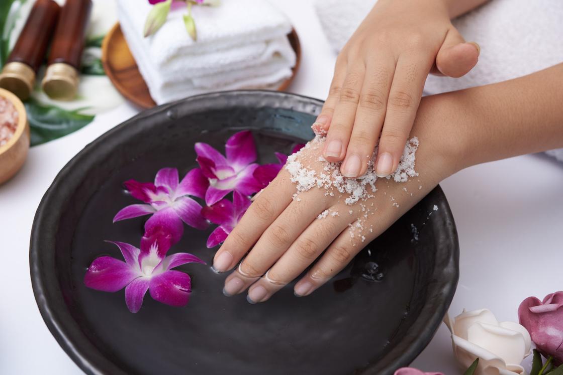 Девушка держит руки в ванночке с морской солью и цветами