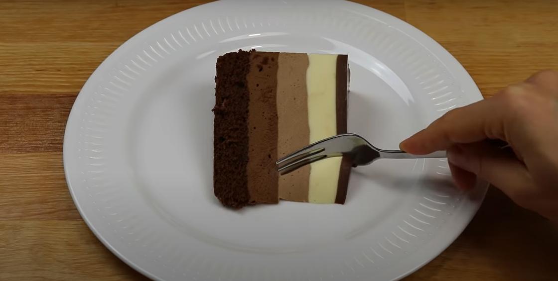 Торт «Три шоколада» на тарелке в разрезе с вилкой