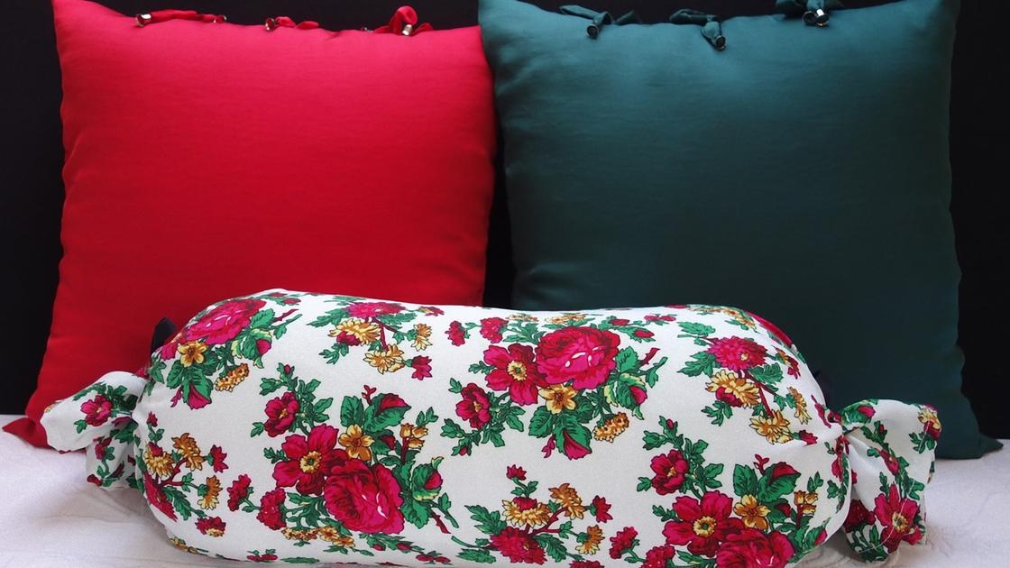 Две квадратные подушки в красной и зеленой наволочке и подушка-валик в наволочке с цветами