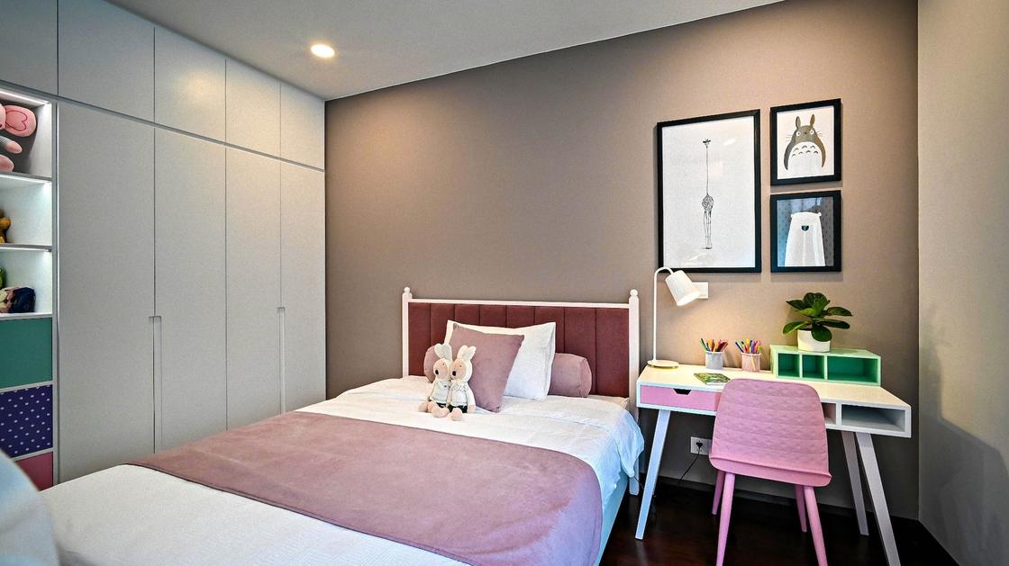 В детской комнате стоит большая белая кровать, рядом стол и розовый стул. Одна стена закрыта шкафом-купе и открытыми полочками , а другая окрашена в бежевый цвет, на стене висят картины в стиле абстракционизма
