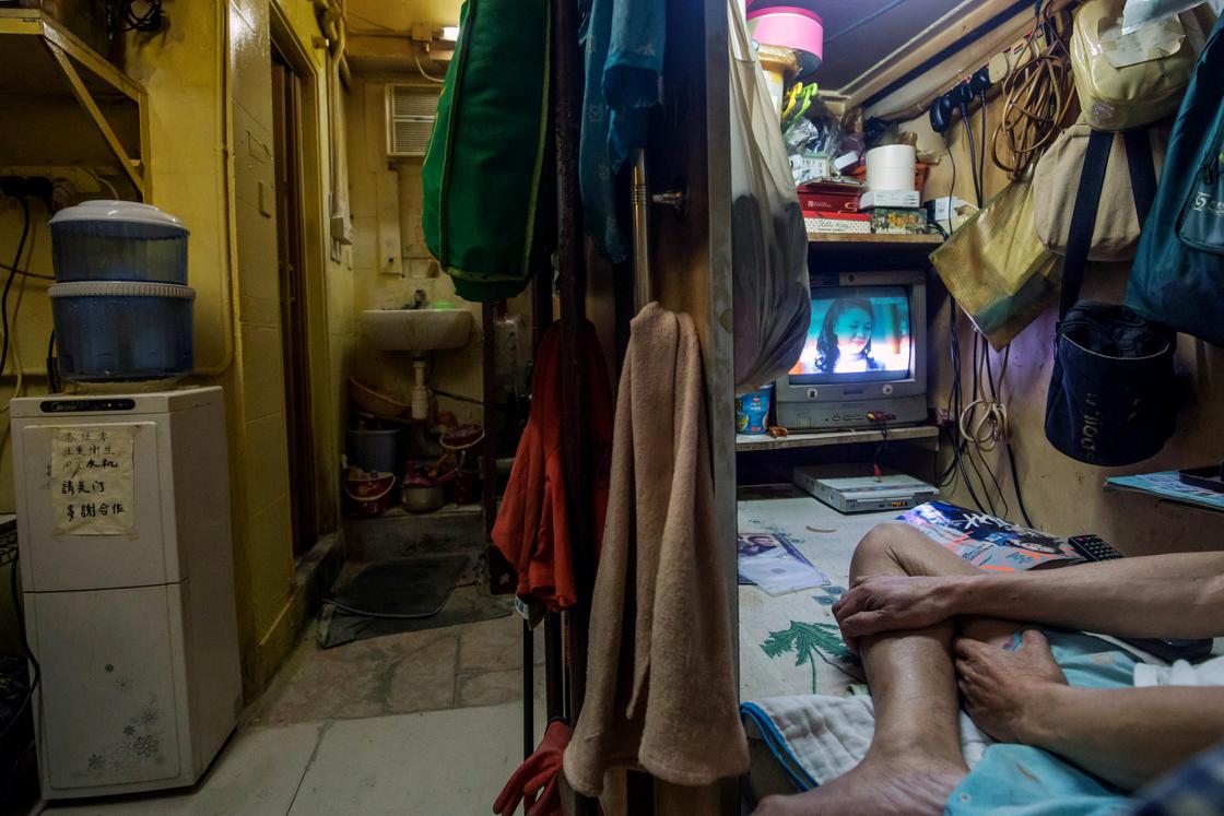 Человек смотрит телевизор в своей 9-метровой квартире в Гонконге