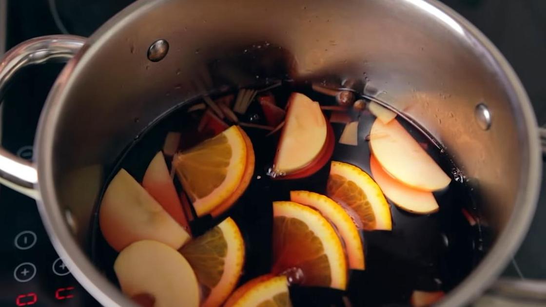 Ломтики яблок и четвертинки апельсина плавают на поверхности красной жидкости похожей на вино