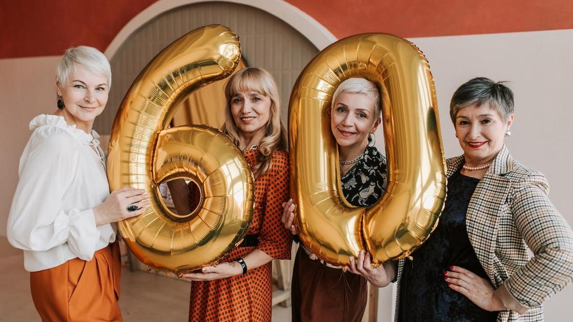 Женщины зрелого возраста с надувными шарами в виде числа 60