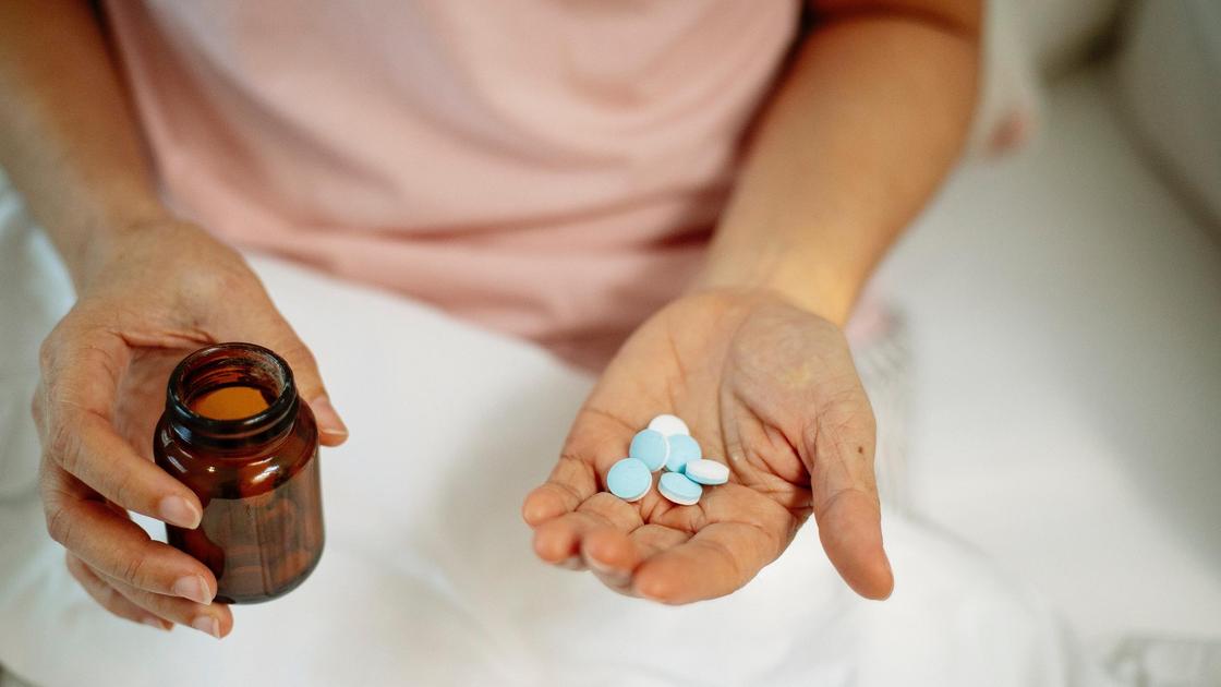 Женщина держит в руках лекарства и бутылек