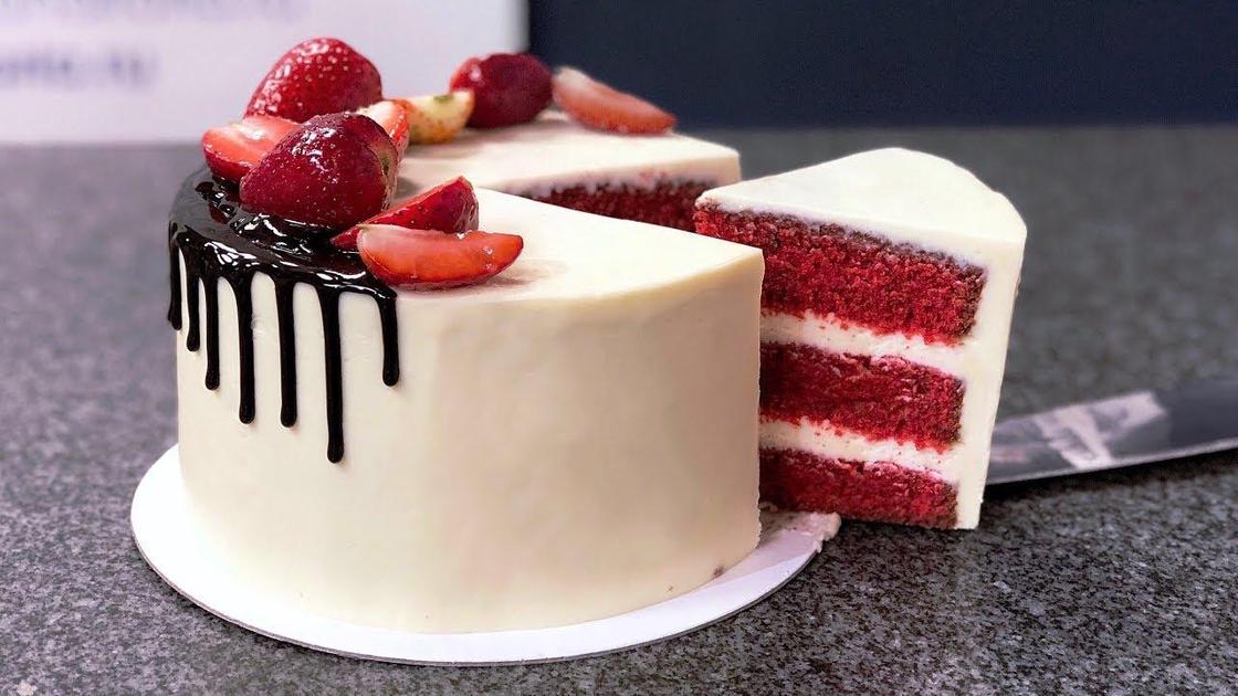 Торт «Красный бархат», украшенный глазурью и клубникой. с отрезанным от него кусочком