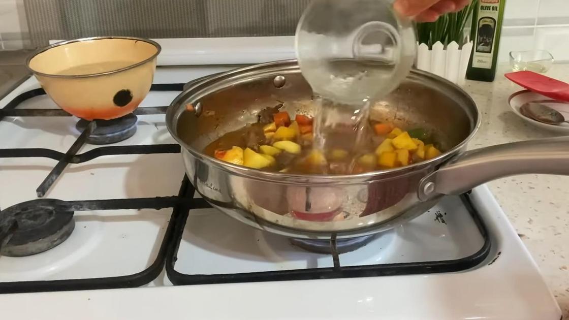 В сковороду с мясом и овощами наливают воду из чашки