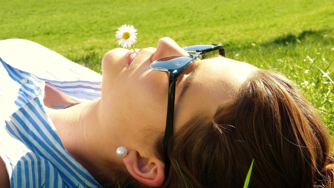 Девушка лежит на траве с ромашкой в зубах