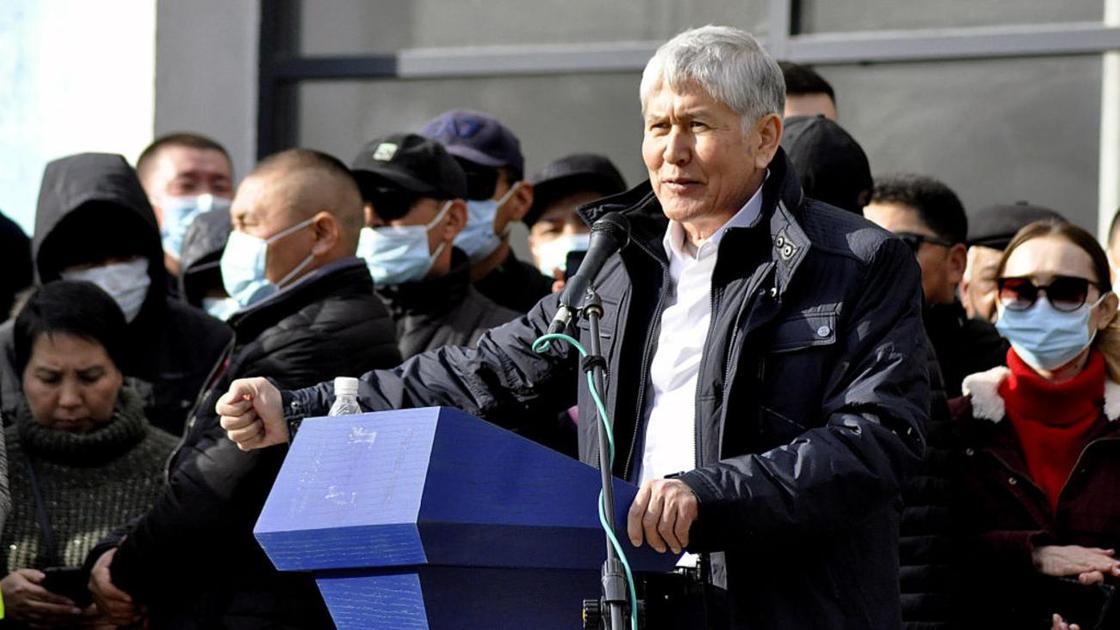 Алмазбек Атамбаев стоит перед трибуной в окружении людей