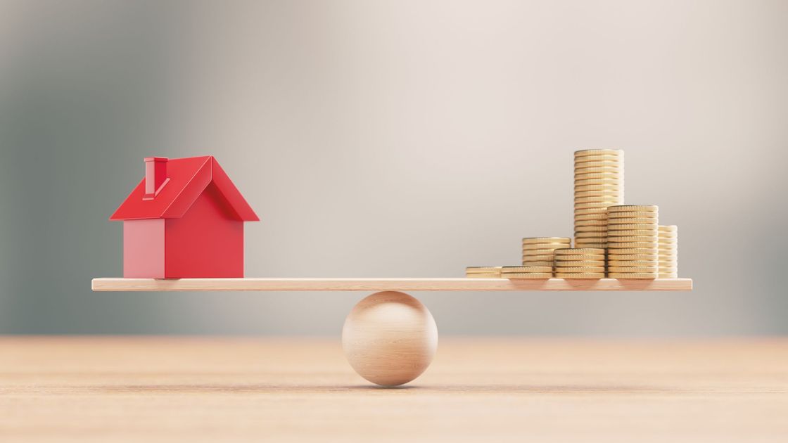 Домик и деньги лежат на импровизированных весах