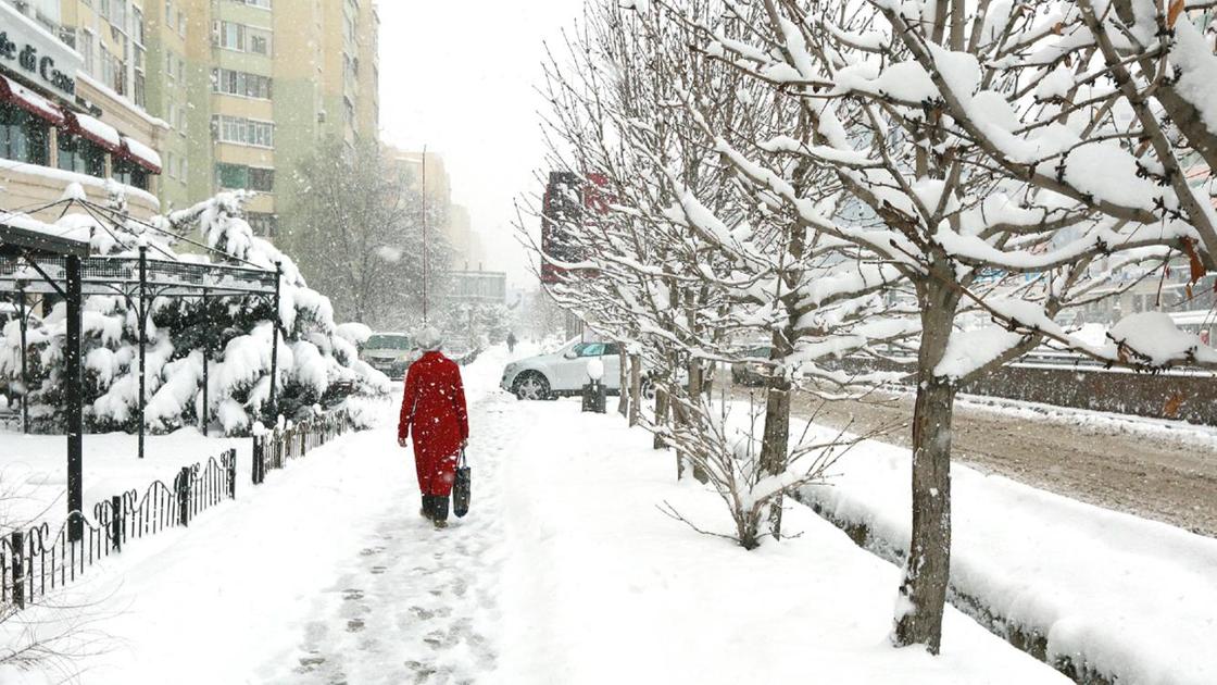 Женщина в красном пальто идет по заснеженной улице