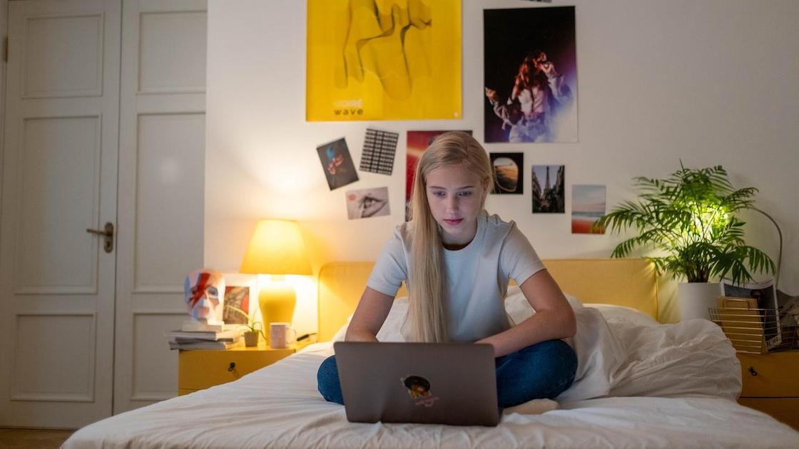 Девочка-подросток сидит в кровати с ноутбуком