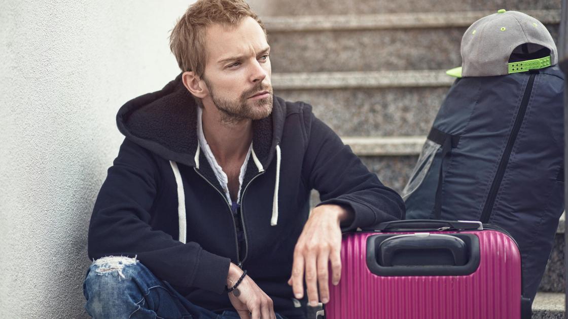 Мужчина с чемоданом и рюкзаком сидит на ступеньках с задумчивым видом