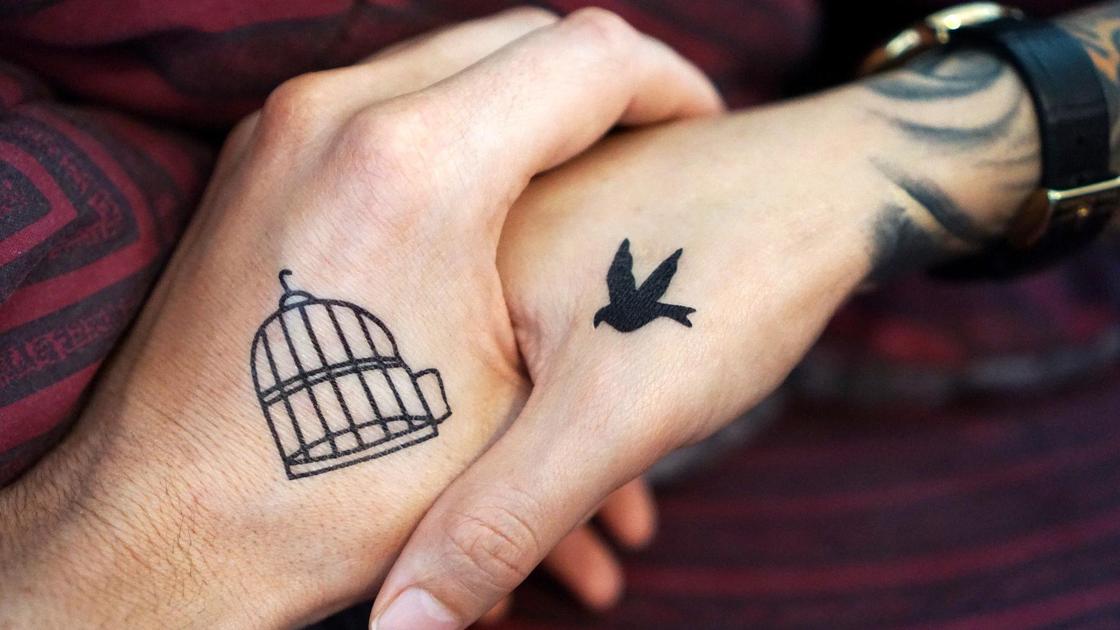 Руки с татуировкой клетки и птички