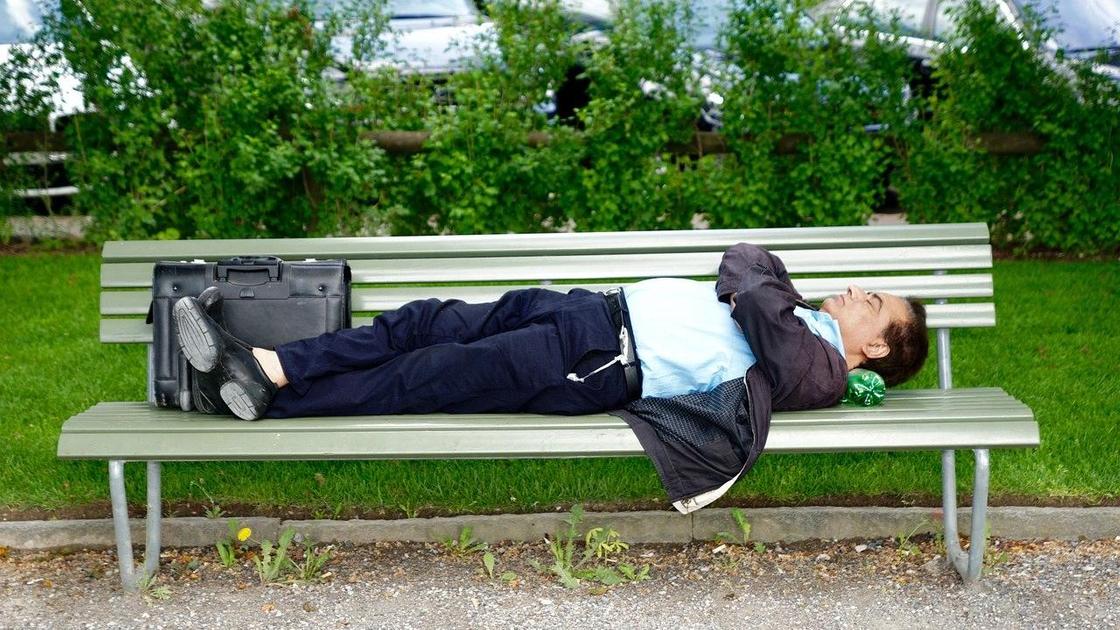 Мужчина лежит на скамейке в парке