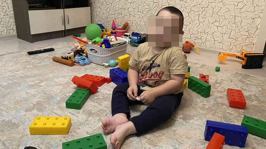 Мальчик сидит на полу среди игрушек