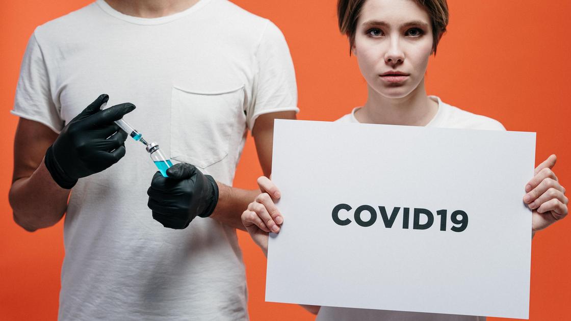 Девушка с плакатом COVID-19 и парень с инъекцией Девушка с плакатом COVID-19 и парень с инъекцией
