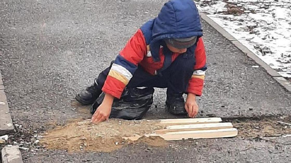 Мальчик заделывает яму на тротуаре