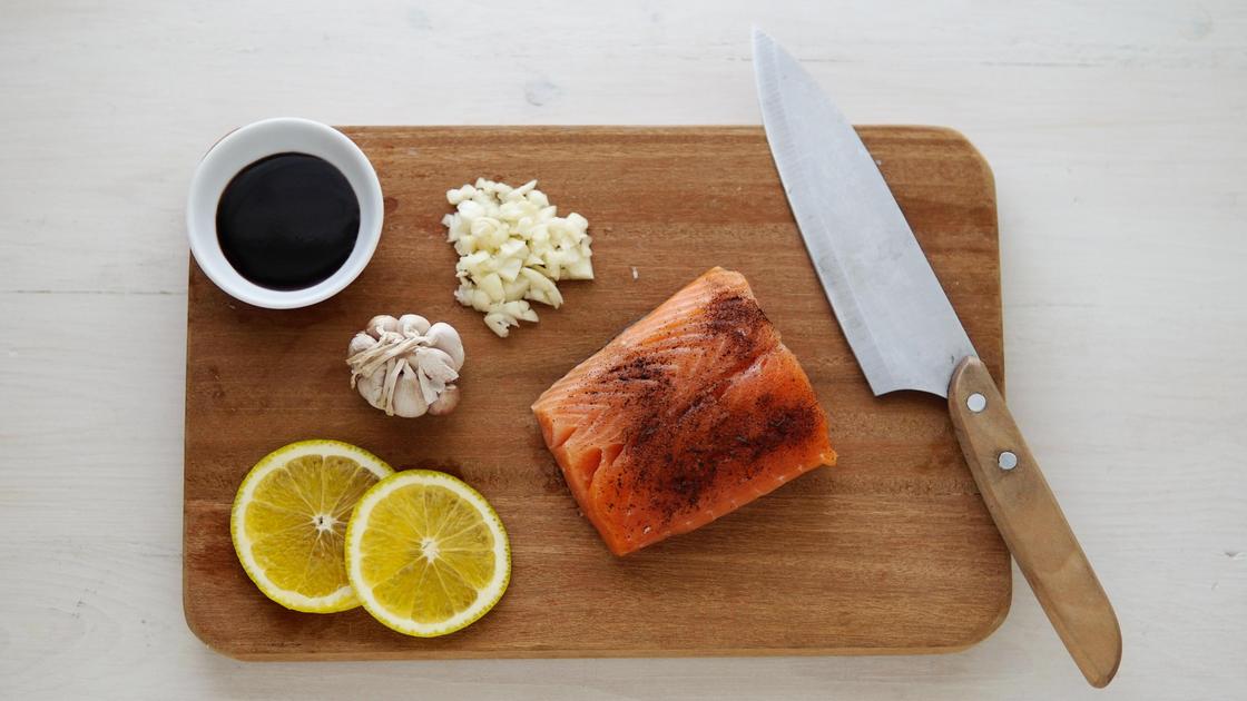 Рыба, чеснок, лимон, соевый соус и нож на доске